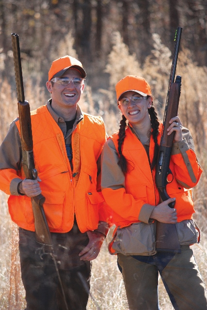 Two hunters in blaze orange holding firearms, carrying hunting rifles safely concept. 