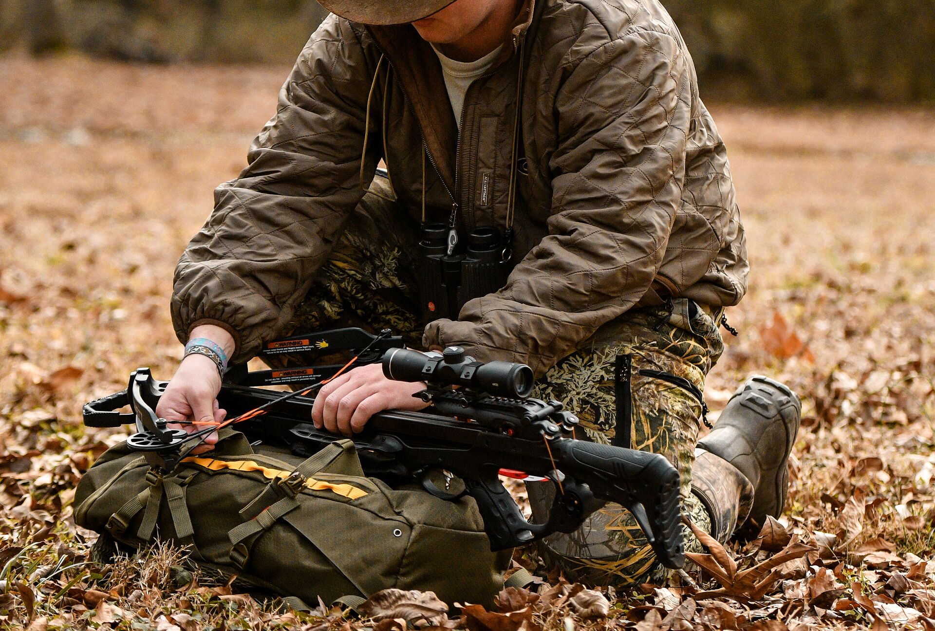 A hunter handles a crossbow while kneeling on the ground