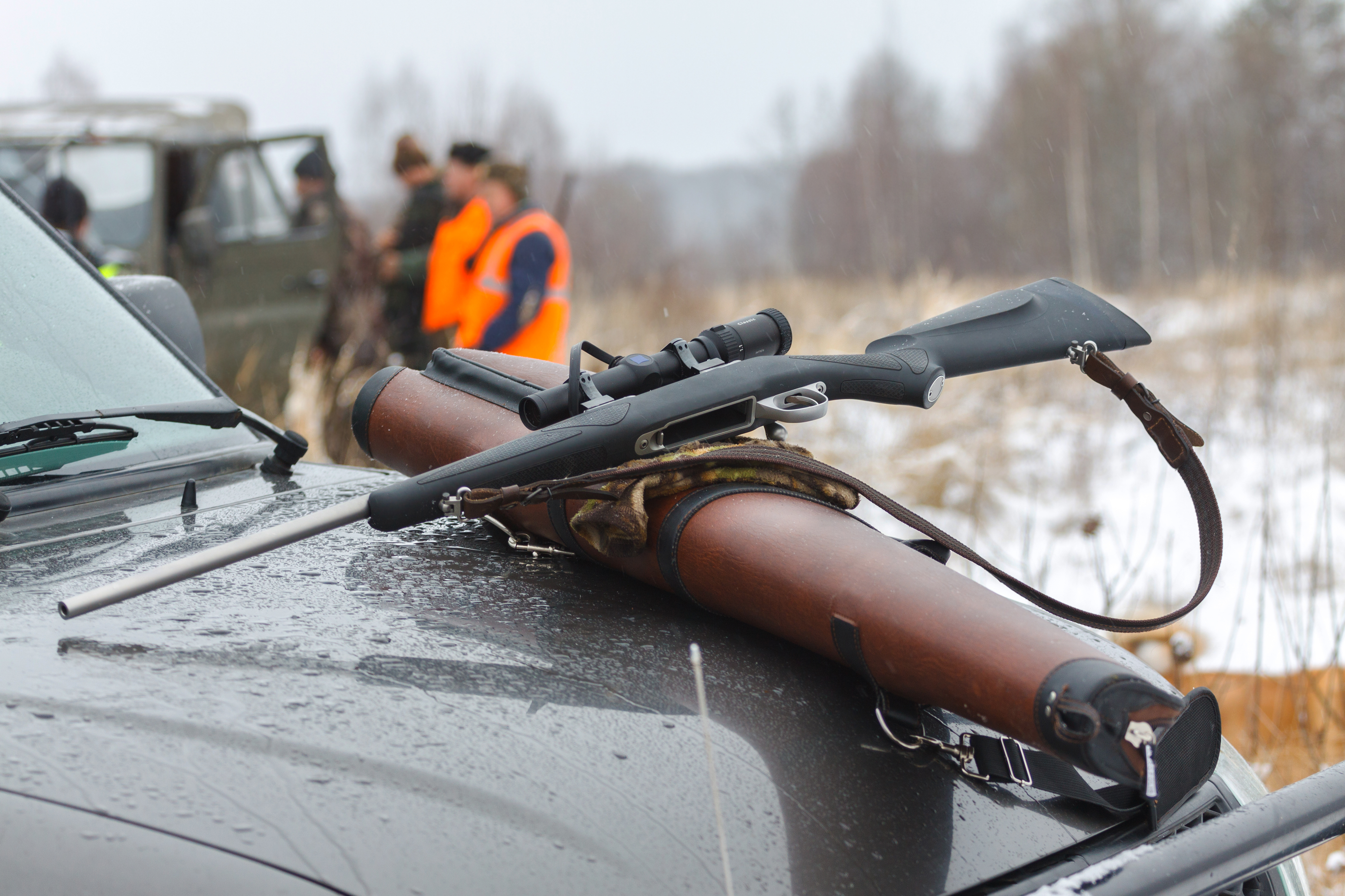 A rifle laying on a truck with hunters in the background, hunters firearms. 