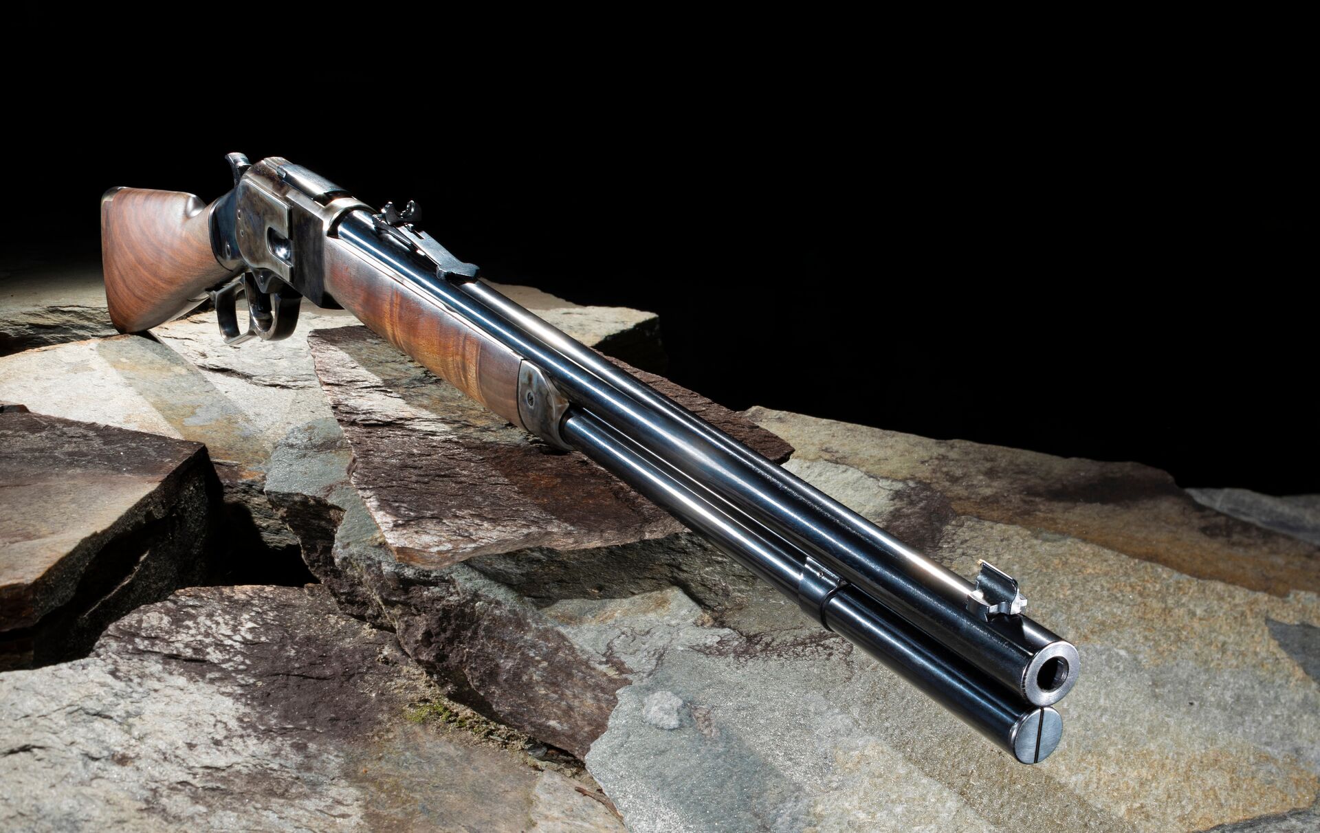 A lever action rifle sits on a stone table top. 