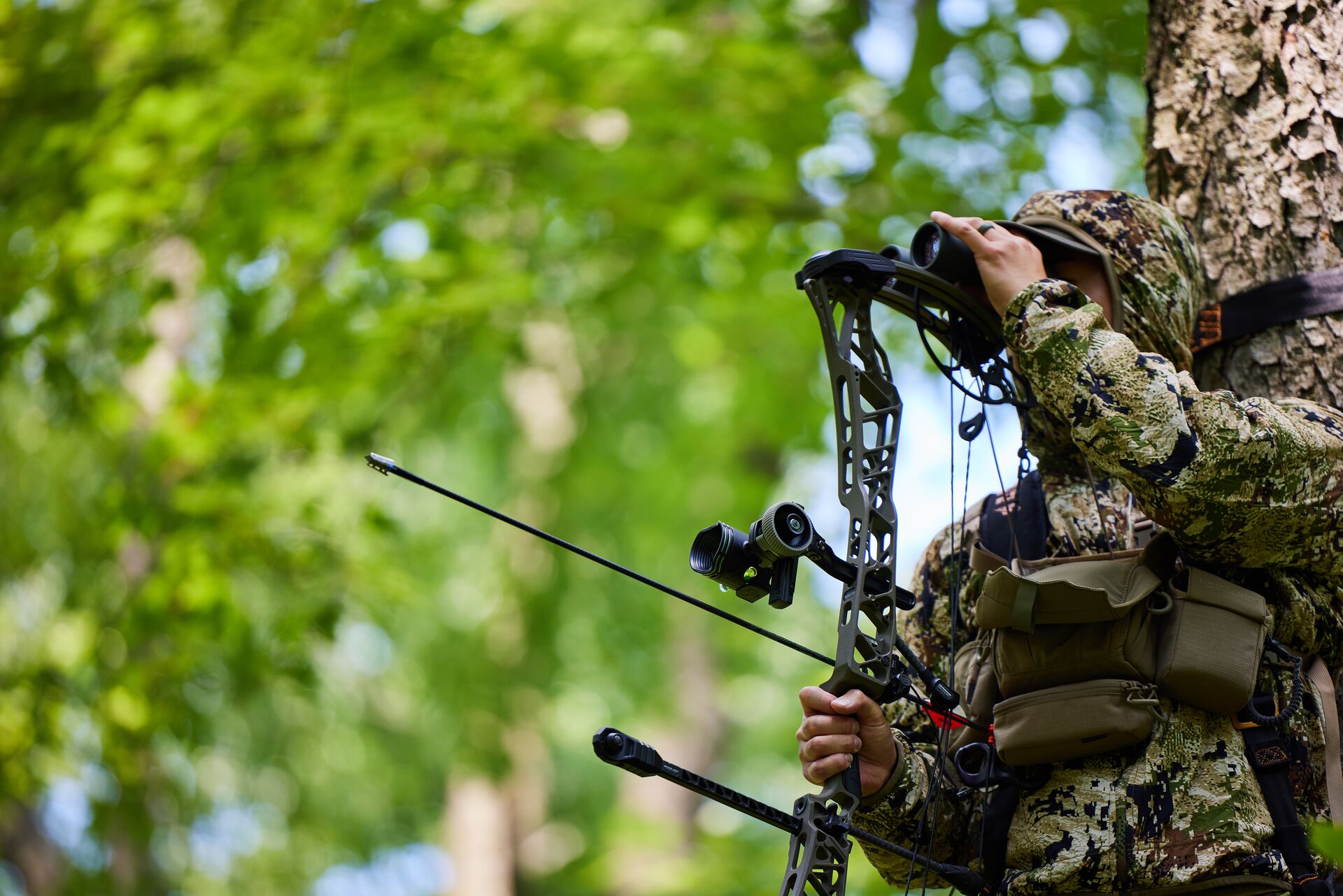 A hunter in camo holding a bow loaded with a broadhead arrow. 