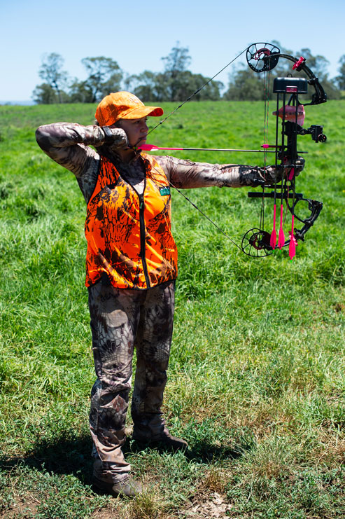 A bowhunter wearing blaze orange and camo aims a compound bow, choosing broadheads concept. 