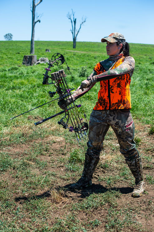 A female bowhunter in blaze orange holds a bow, bowhunting and broadheads safety concept. 