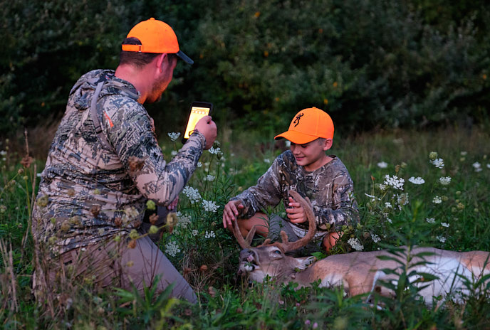 A man takes a picture of a boy with a deer after the shot, venison concept. 