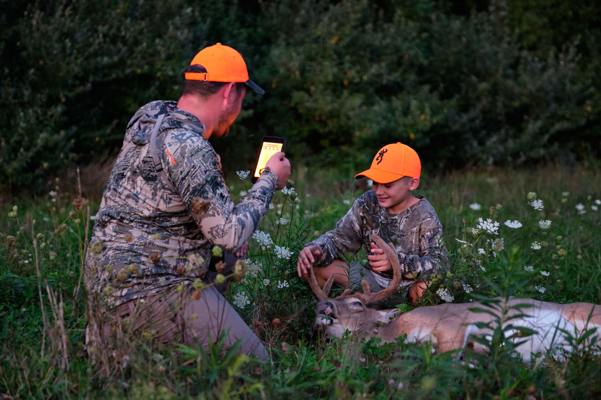  A man takes a photo of a young hunter with a buck deer after the kill shot. 