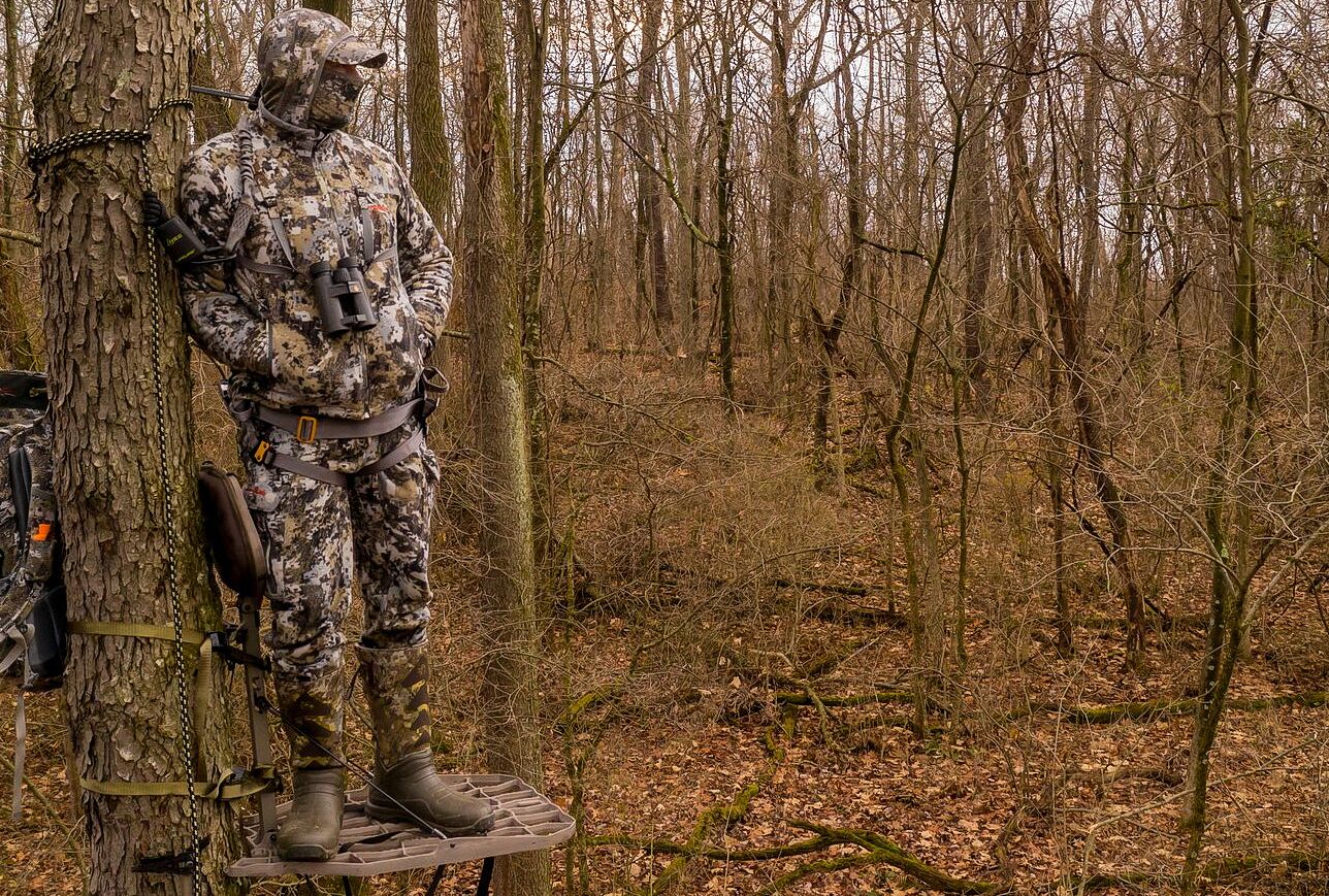 A hunter in camo in a tree wearing hunting boots. 