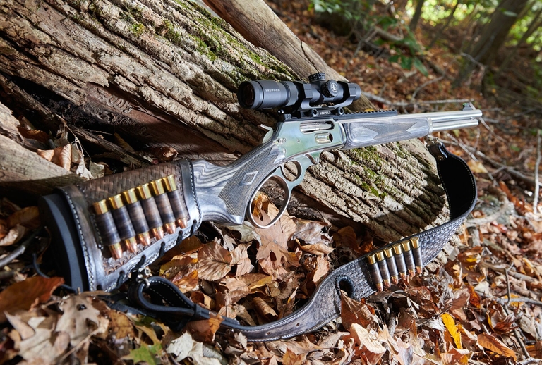 A tactical lever action rifle leans against a log on the ground.