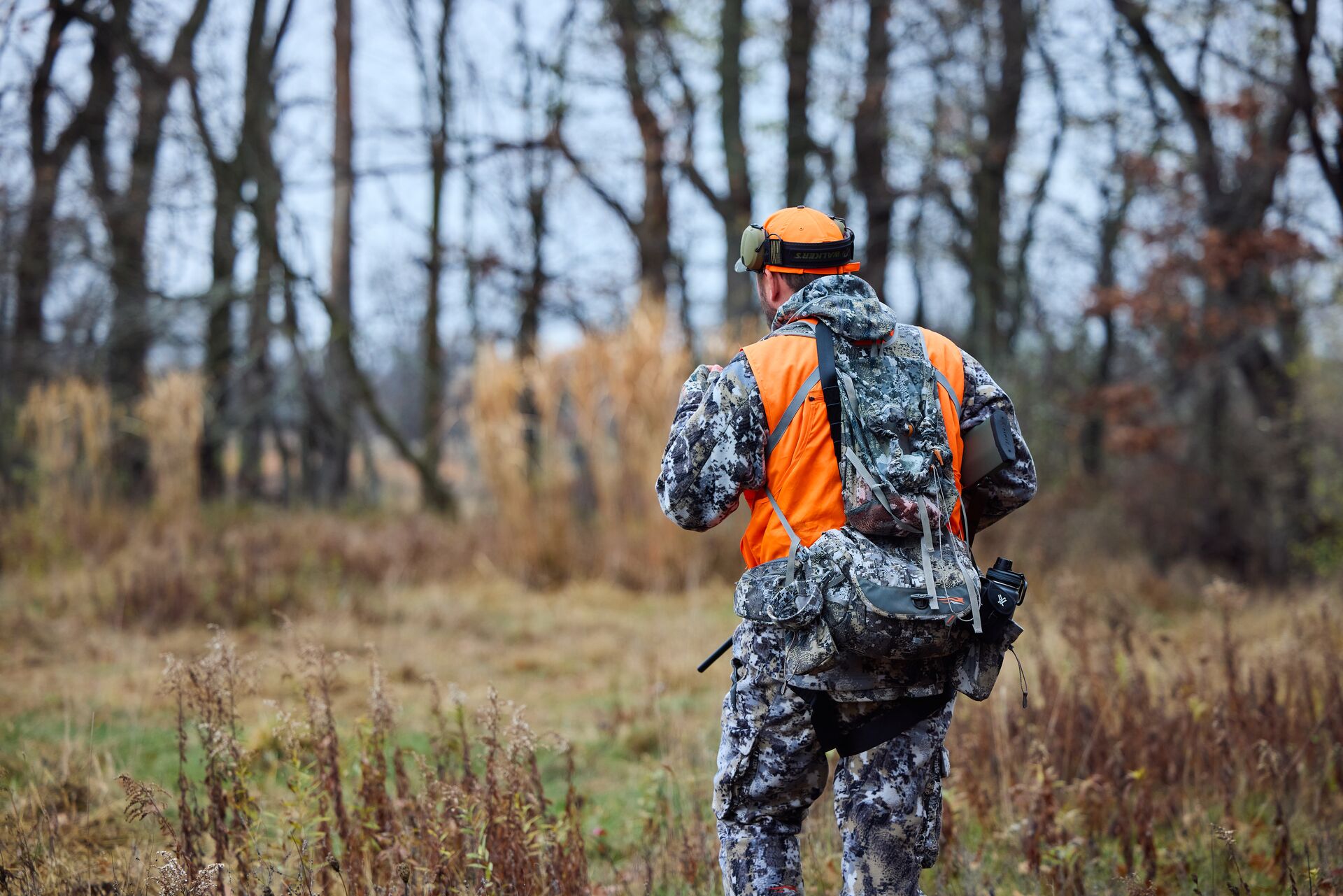 A hunter wears camo and blaze orange with a hunting pack.