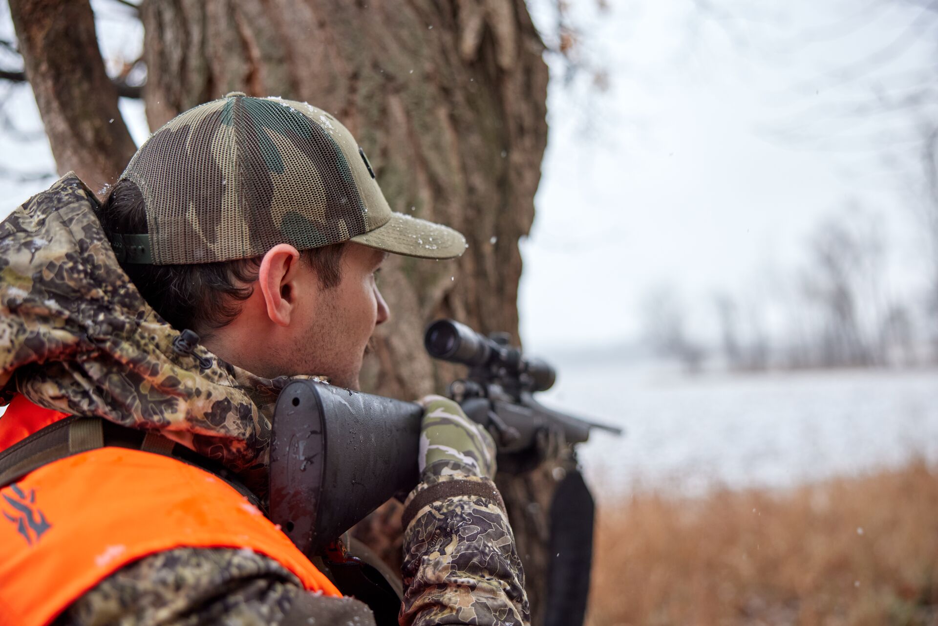 A hunter in blaze orange and camo aims a rifle, how to get into hunting concept. 