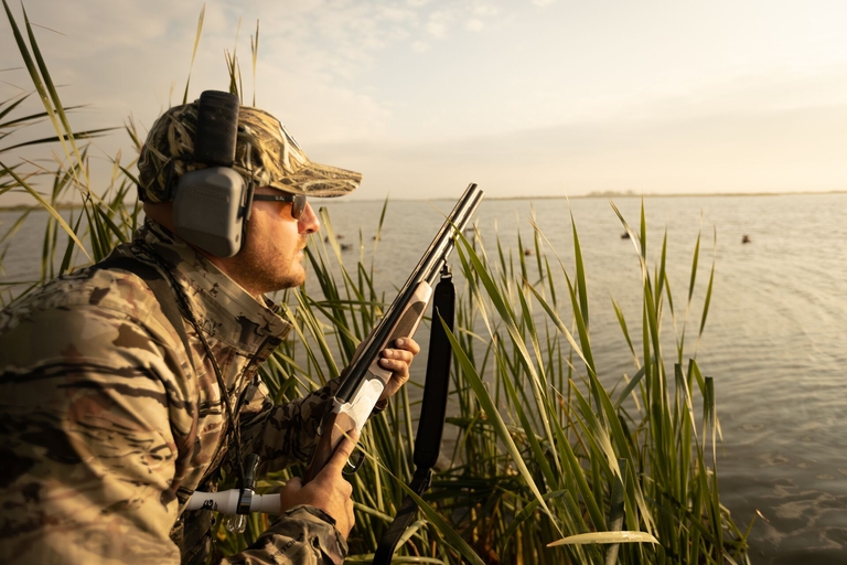 A duck hunter waits in the reeds, how does hunting help wildlife conservation concept. 