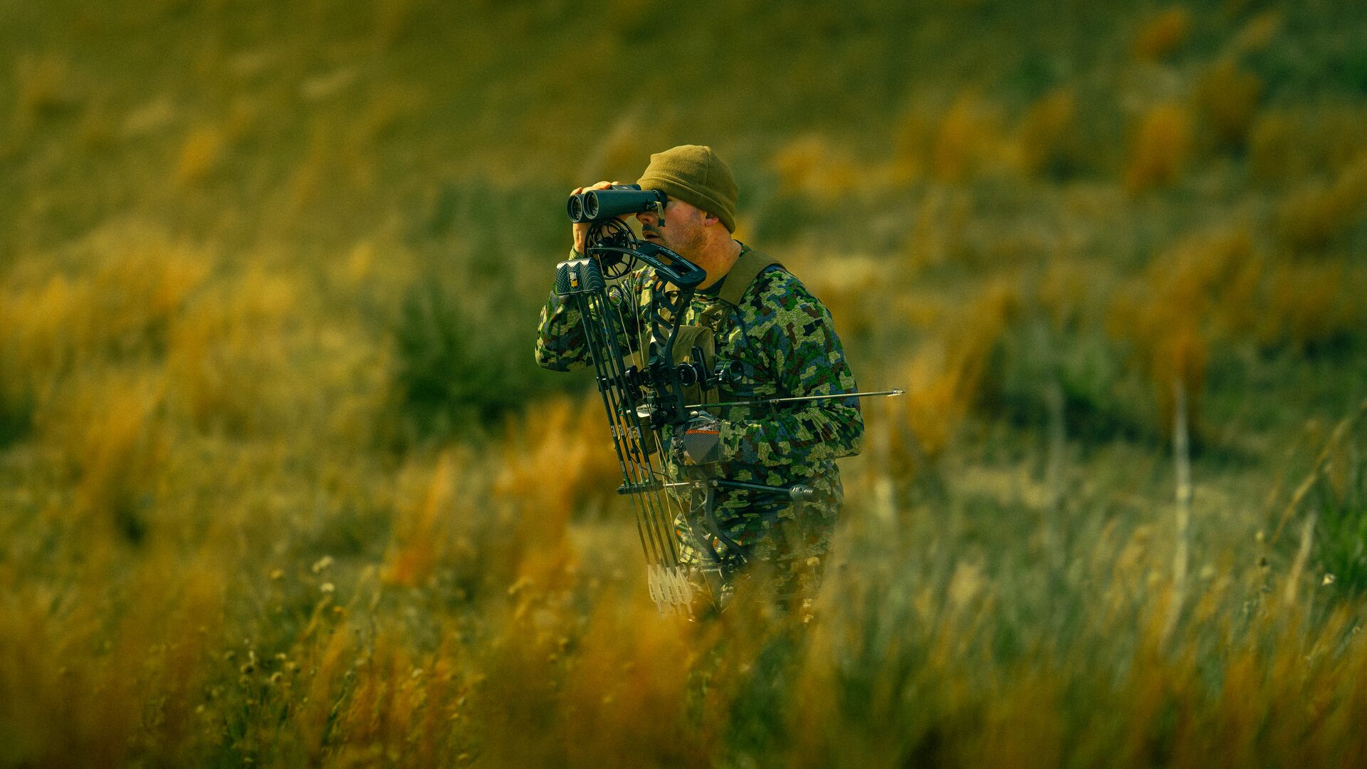Hunter with a bow using binoculars. 