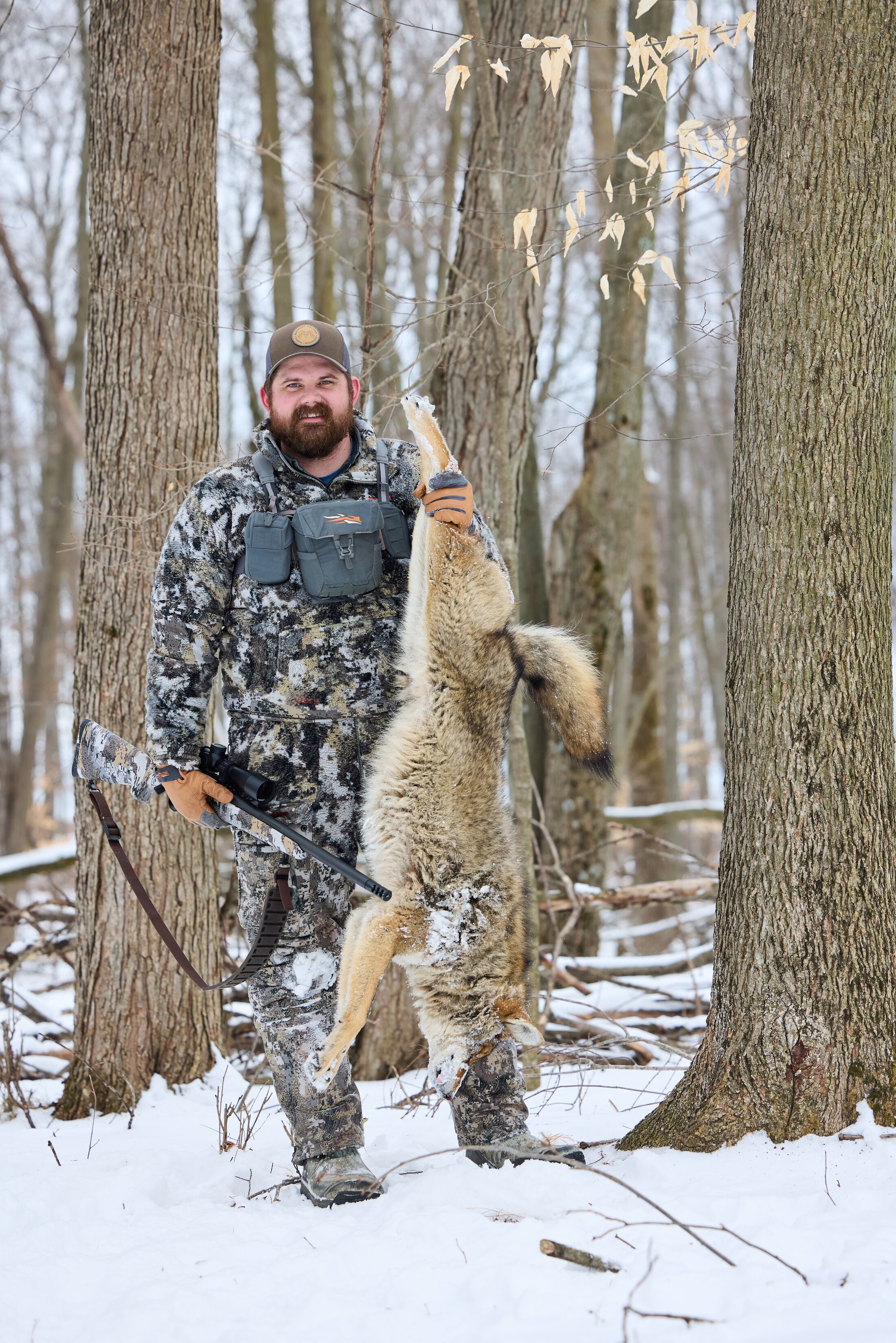 Hunter in the snow holds up coyote after hunt, how to get into hunting concept. 