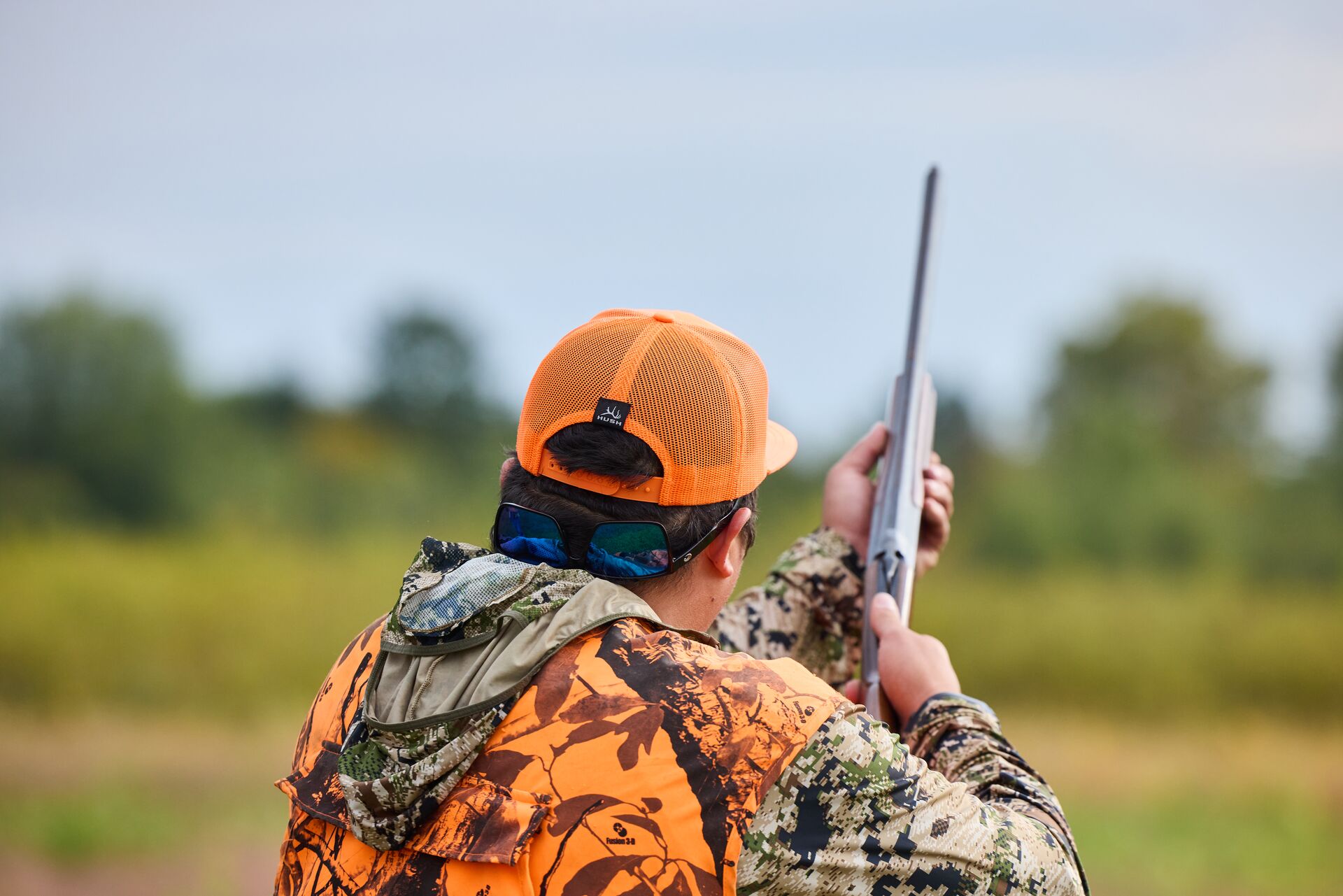 Hunter in blaze orange aims shotgun, pheasant hunting without a dog concept.