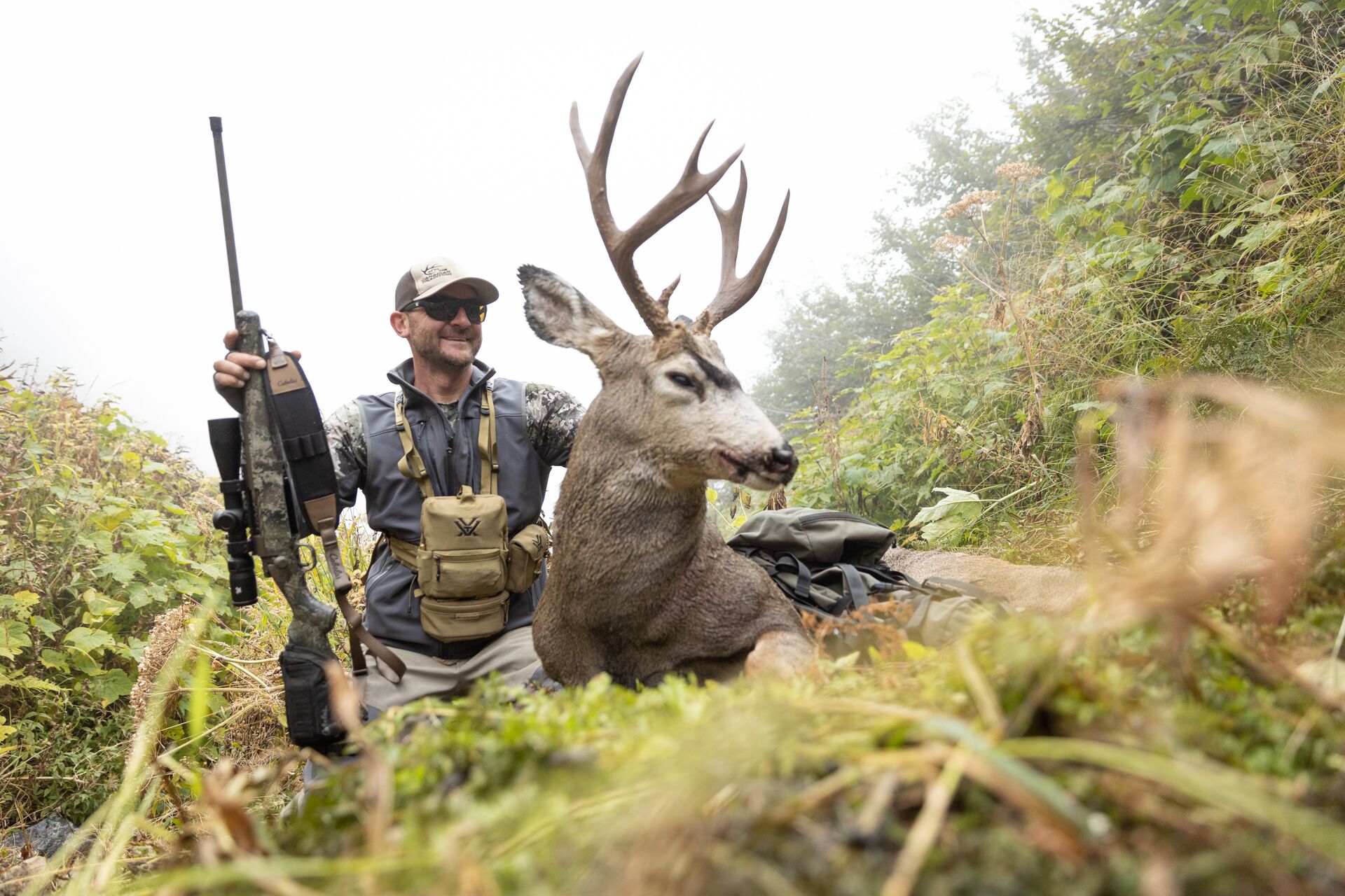 Hunter with rifle and buck deer after hunt. 