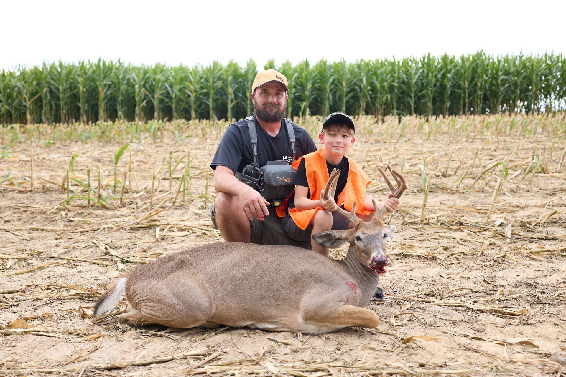 Man and boy wearing blaze orange pose with deer after hunt, Florida hunter education course concept.