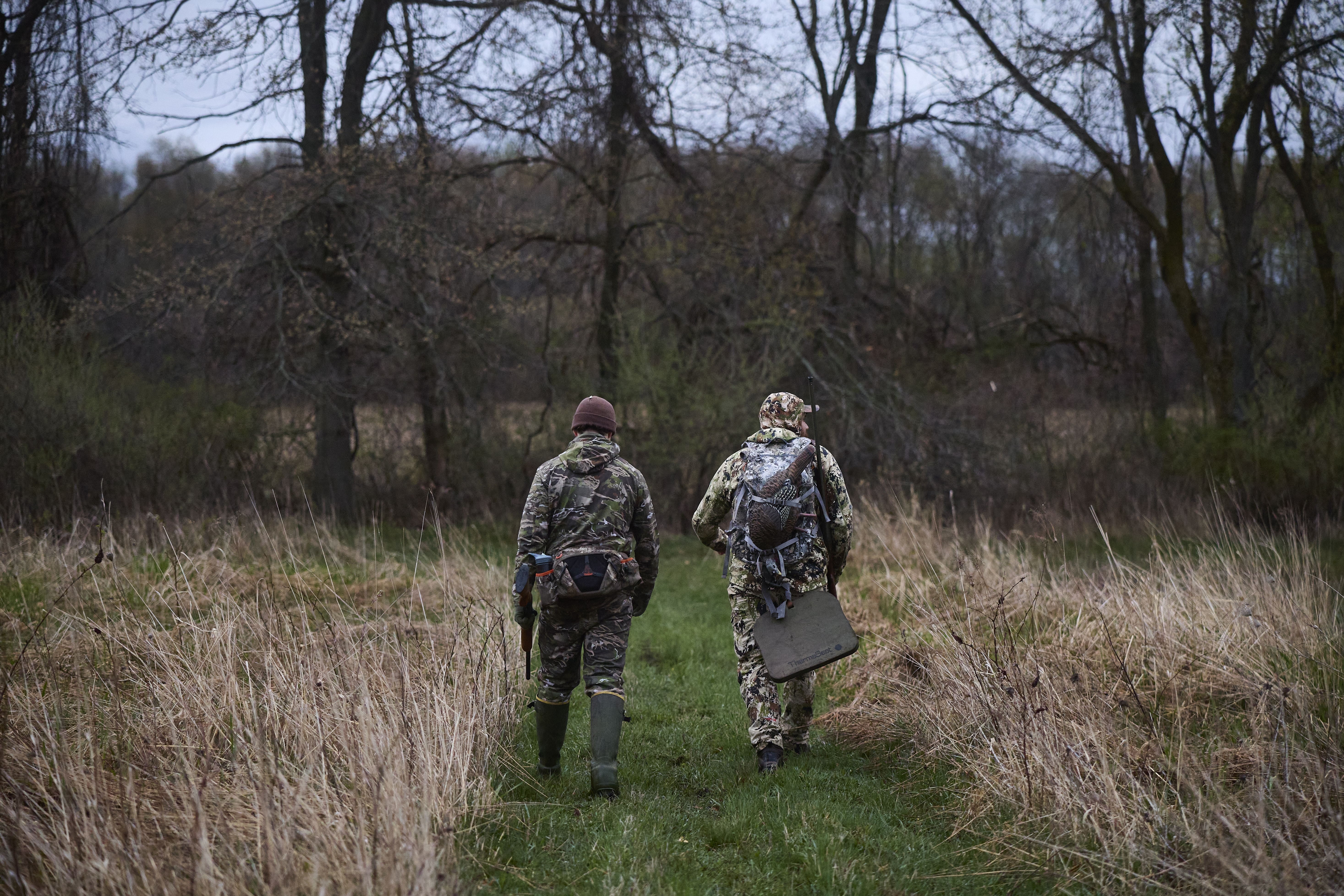 Hunters walking into the woods with hunting gear. 