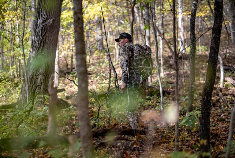 A hunter in the woods with a hunting gear pack. 