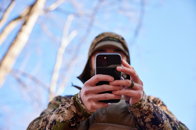 A hunter uses a cellphone in the field, hunting education concept. 